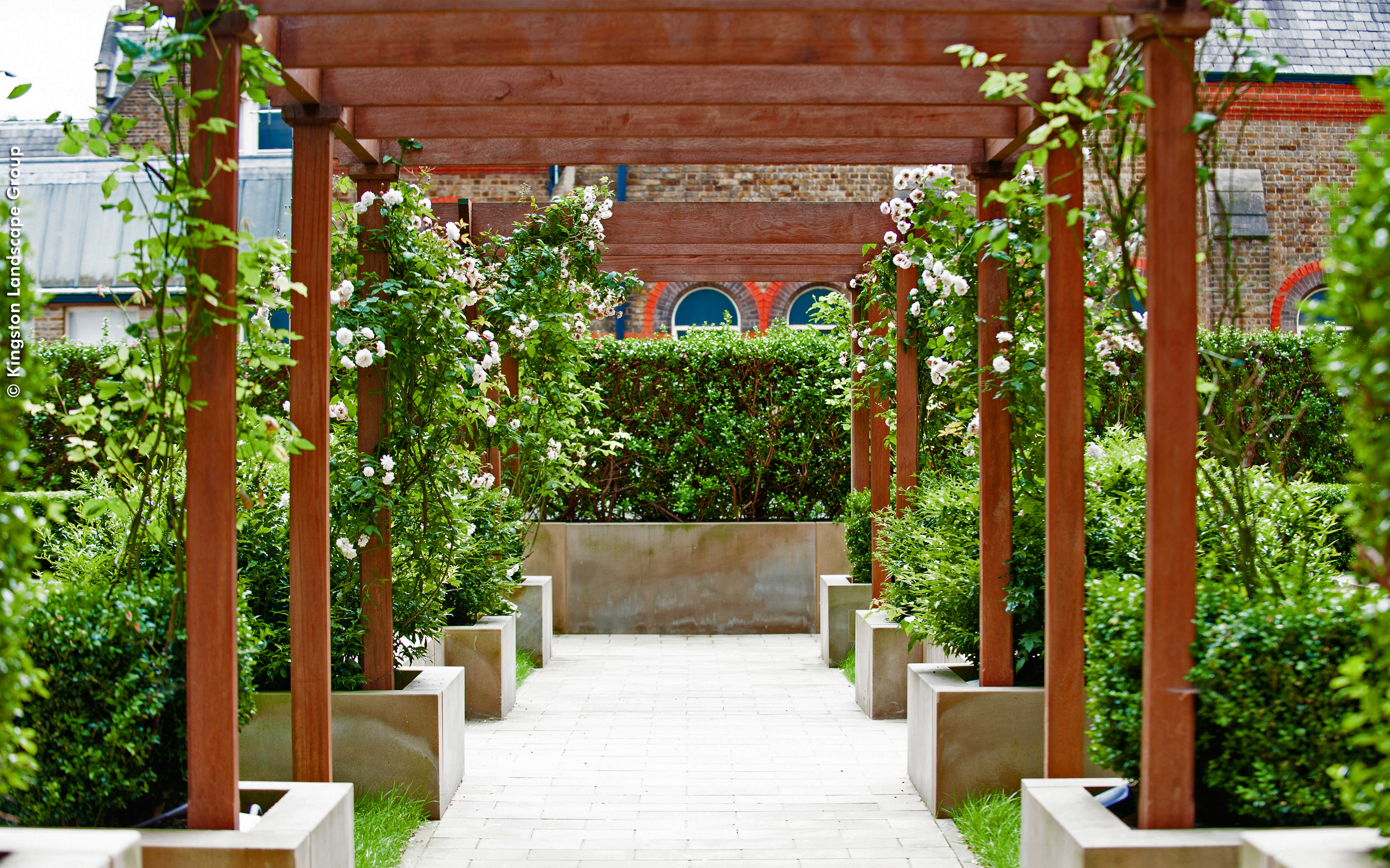 A wooden pergola enhances the courtyard and enables the growth of flowering creepers. A wooden pergola with creepers and planters